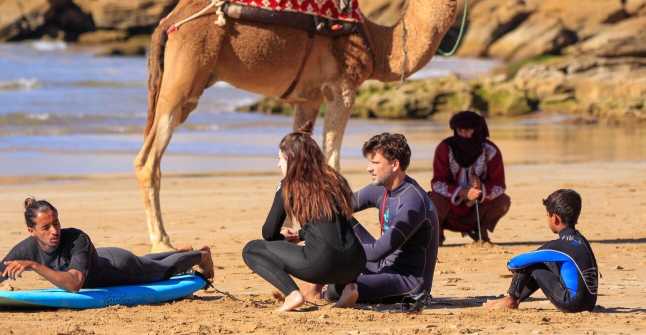 A group of beginners taking surf lessons in Tamraght, Morocco, learning to ride the waves at Paddle Out Morocco Surfhouse.
